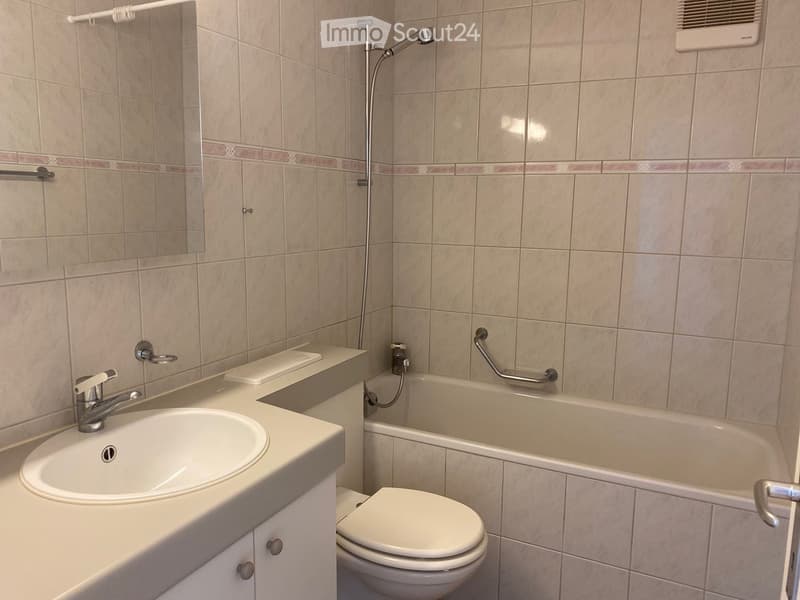 Bathroom with beige tiled walls, a white sink with a chrome faucet, a bathtub with a handheld showerhead, a toilet, and a mirror above the sink.