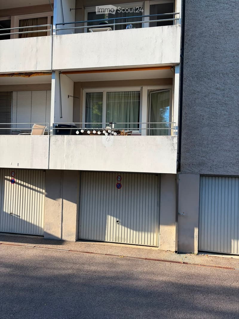 Two-story residential building with balconies, large windows, and a covered entrance area.