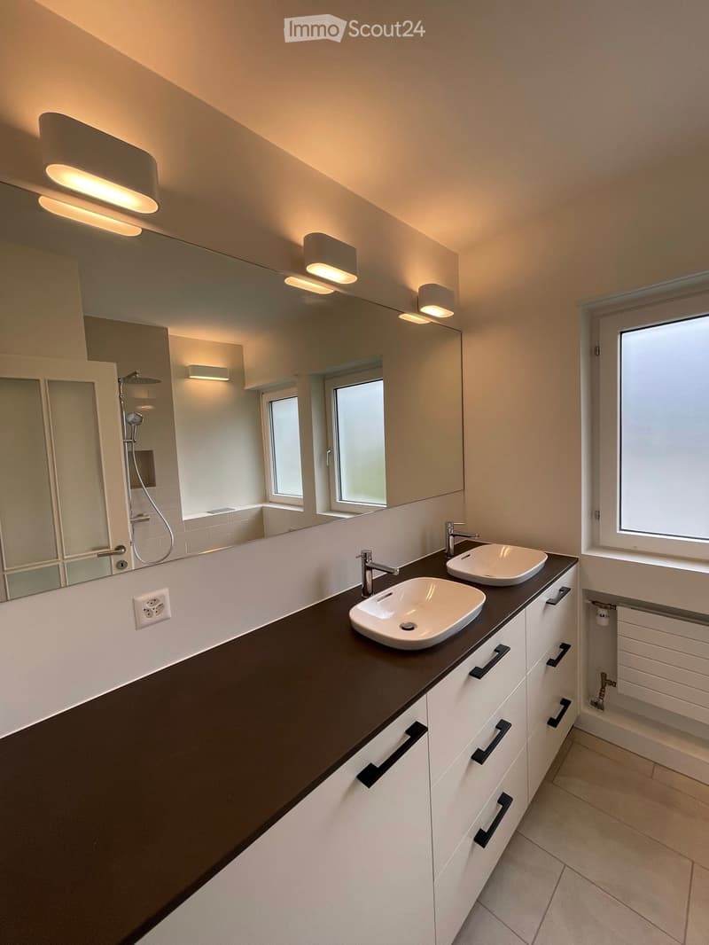 Modern bathroom with two sinks, sleek dark countertop, white cabinets, large mirror, and built-in shower area.