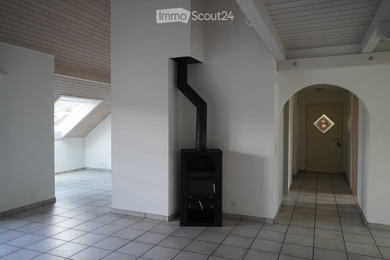 Bright hallway with tiled floor, white walls, and a wood-burning stove with chimney. Features an arched doorway leading to another room and a skylight above.