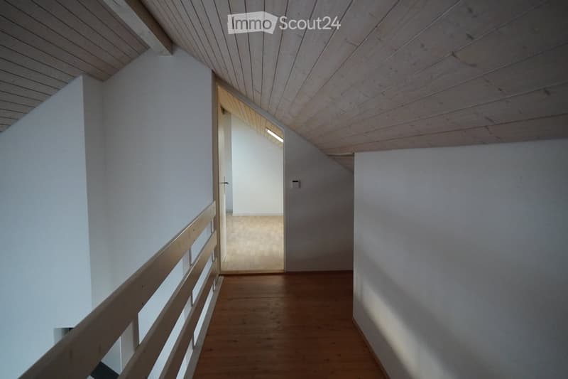 Modern hallway with wooden flooring, white walls, and a wooden railing leading to an open space.