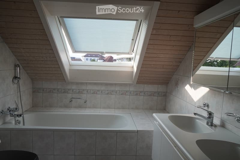 Modern bathroom with a skylight window, wooden ceiling, tiled walls, bathtub, sink, and mirror.