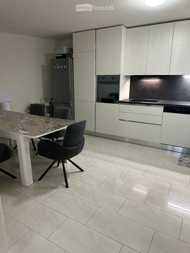 Modern kitchen with white cabinets, stainless steel appliances, a dining table with chairs, and tiled flooring.