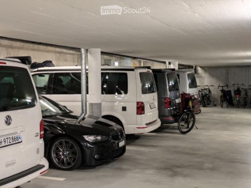 Underground parking area with several parked cars and bicycles, concrete walls and ceiling, organized parking spaces.