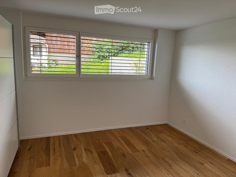 Empty room with light wooden flooring, white walls, and large windows with blinds. No furniture or equipment present.