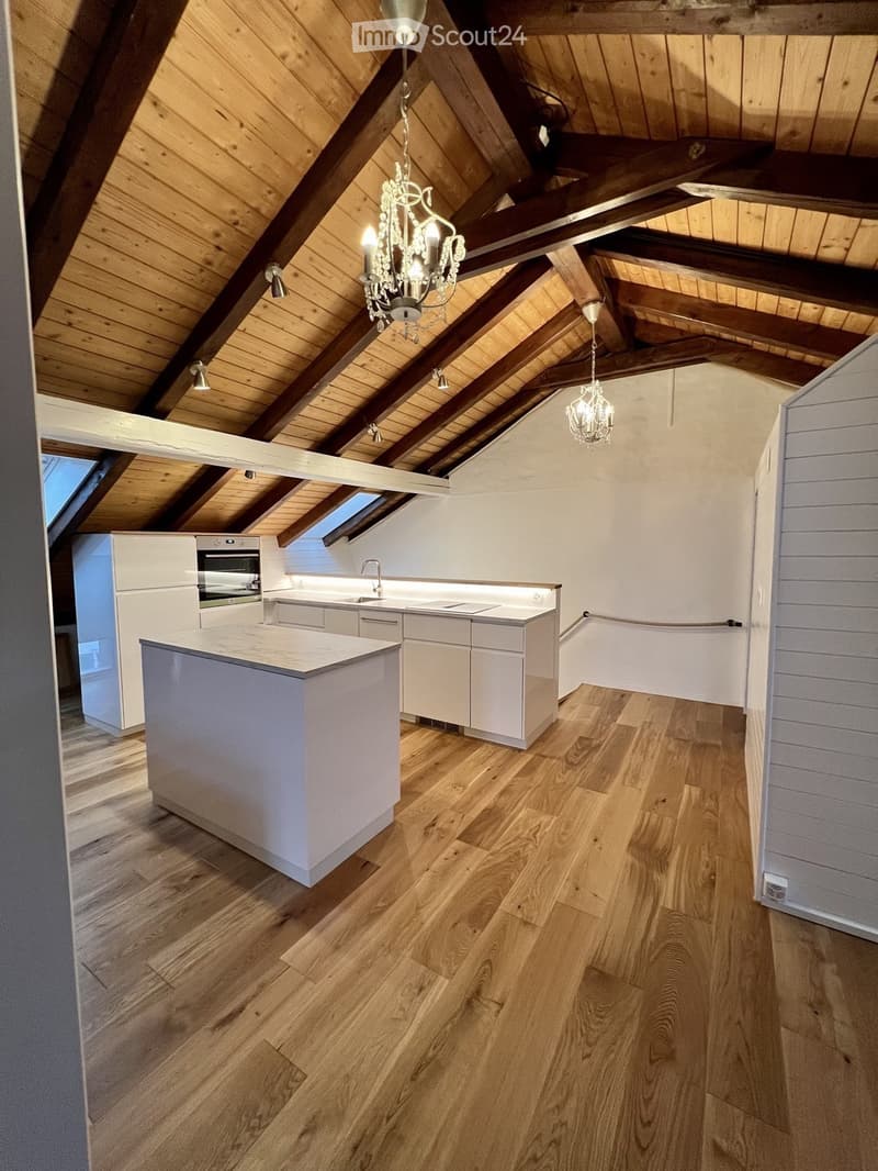 Modern kitchen with white cabinets, a central island, and wooden flooring. Exposed wooden beams and a chandelier adorn the vaulted ceiling.