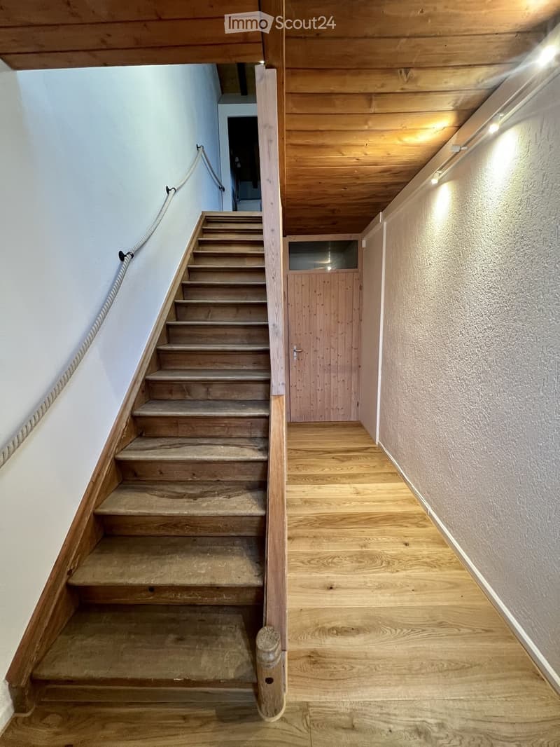 Wooden staircase with a handrail, wooden floor, and a wooden door at the end of the hallway.