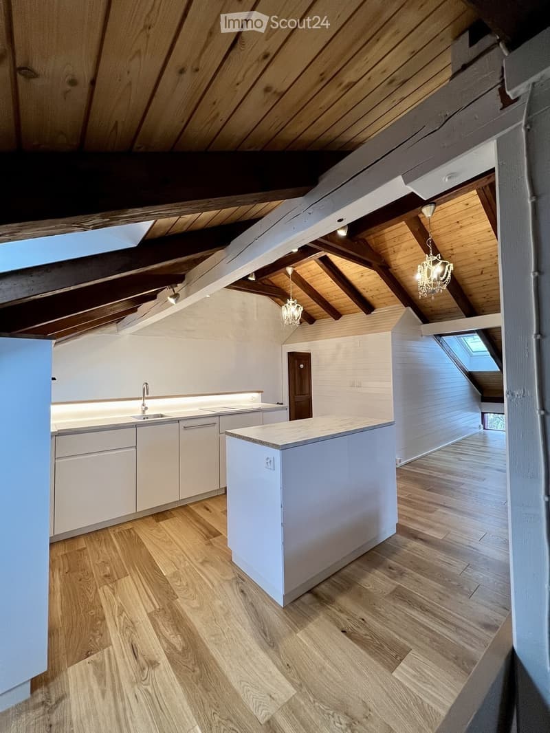 Modern kitchen with white cabinets, a central island, and wooden flooring. Features a sink with a faucet, built-in lighting, and exposed wooden beams on the ceiling.