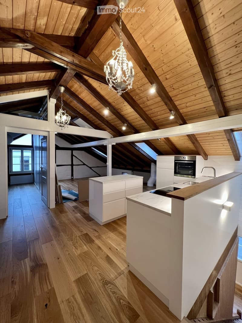 Modern kitchen with wooden floors, white cabinets, a central island, and exposed wooden beams on the ceiling.