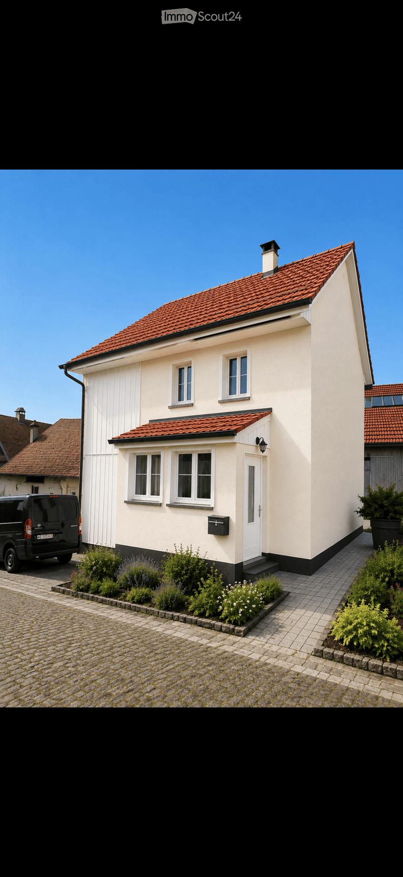 Single-story house with white walls, red-tiled roof, multiple windows, and a small garden area with plants and shrubs.