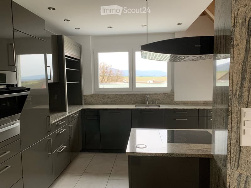Modern kitchen with dark grey cabinets, granite countertops, stainless steel appliances, and large windows overlooking a scenic view.