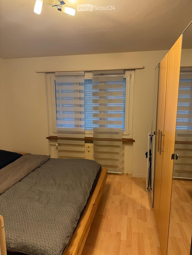 Cozy bedroom with a wooden bed, grey patterned bedding, a radiator, and a wardrobe with mirrored doors.