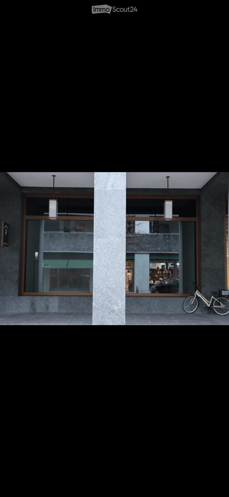 Modern building entrance with large glass windows, hanging pendant lights, and a bicycle parked outside.