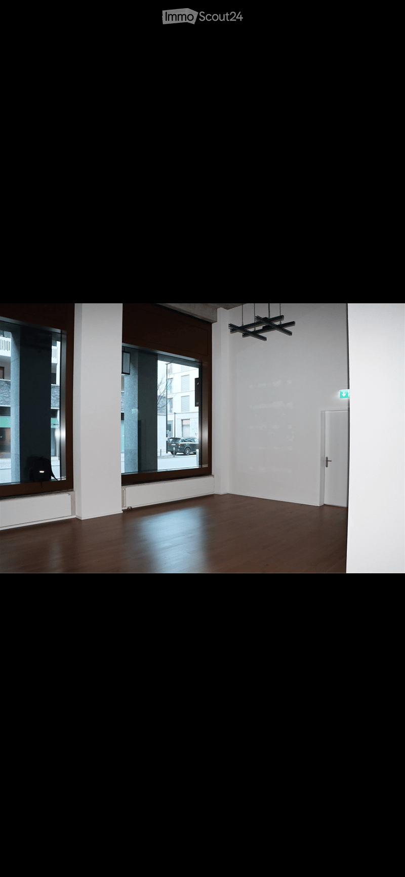 Empty room with wooden flooring, white walls, large windows, and a door. No furniture or equipment present.