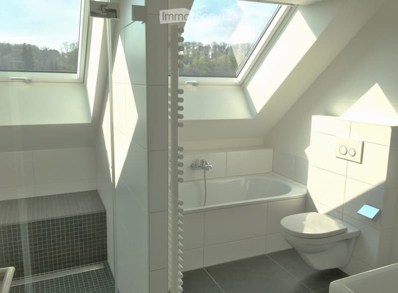 Modern bathroom with a bathtub, toilet, and a glass-enclosed shower area. The room features white tiles, a skylight window, and a sleek shower rail.