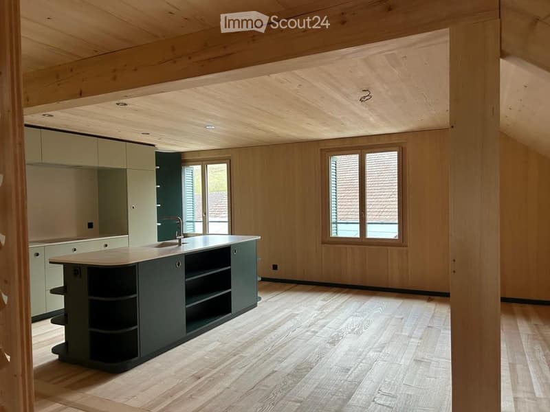 Modern kitchen with light wood walls and ceiling, wooden flooring, central island with sink and faucet, and light green cabinets.