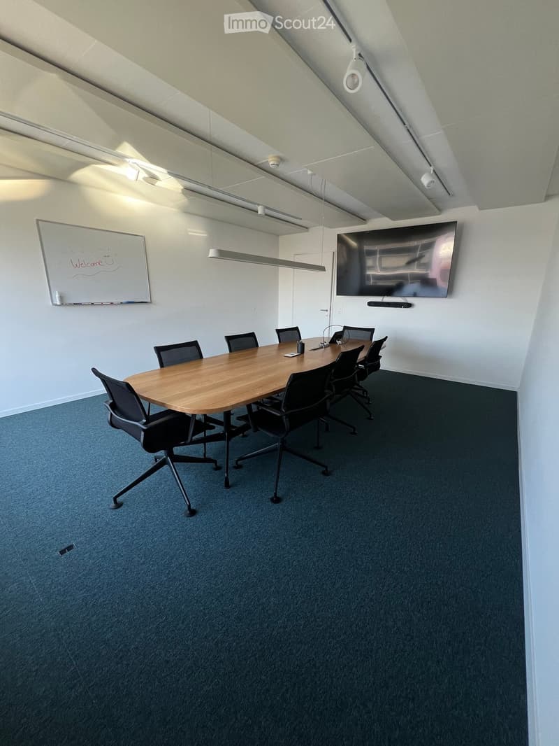 Conference room with a large wooden table, black chairs, a mounted screen, and a whiteboard with a welcome message.