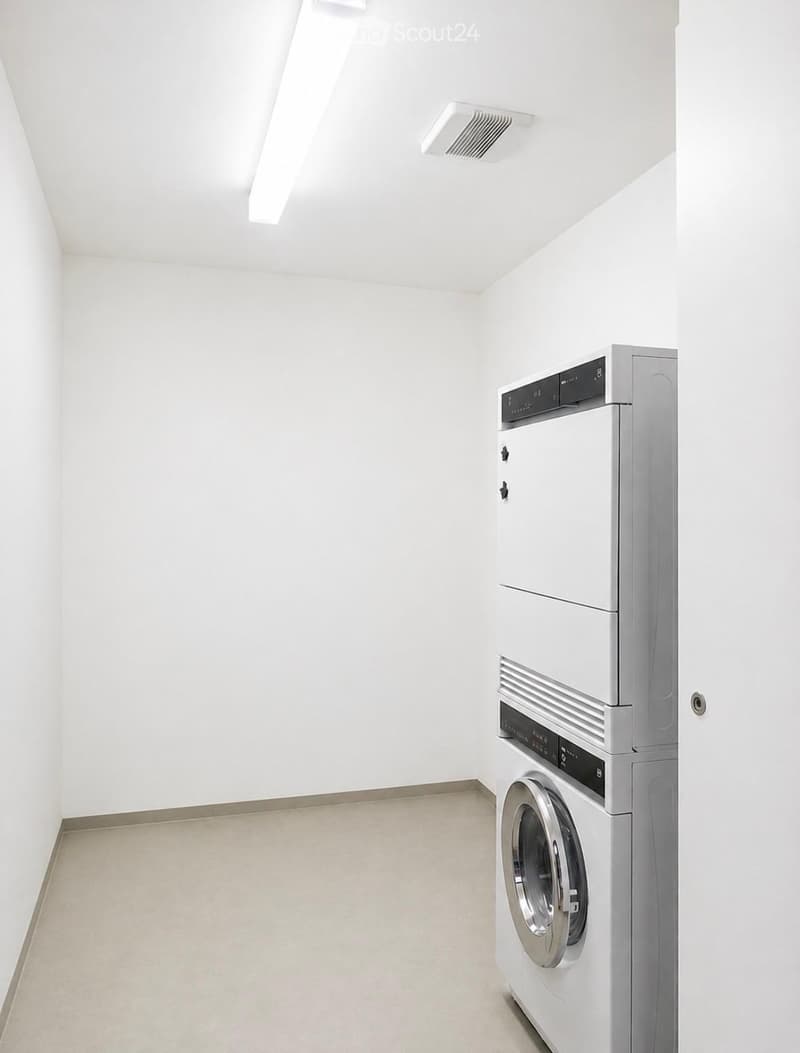 Empty room with white walls and a modern washing machine and dryer unit in the corner.