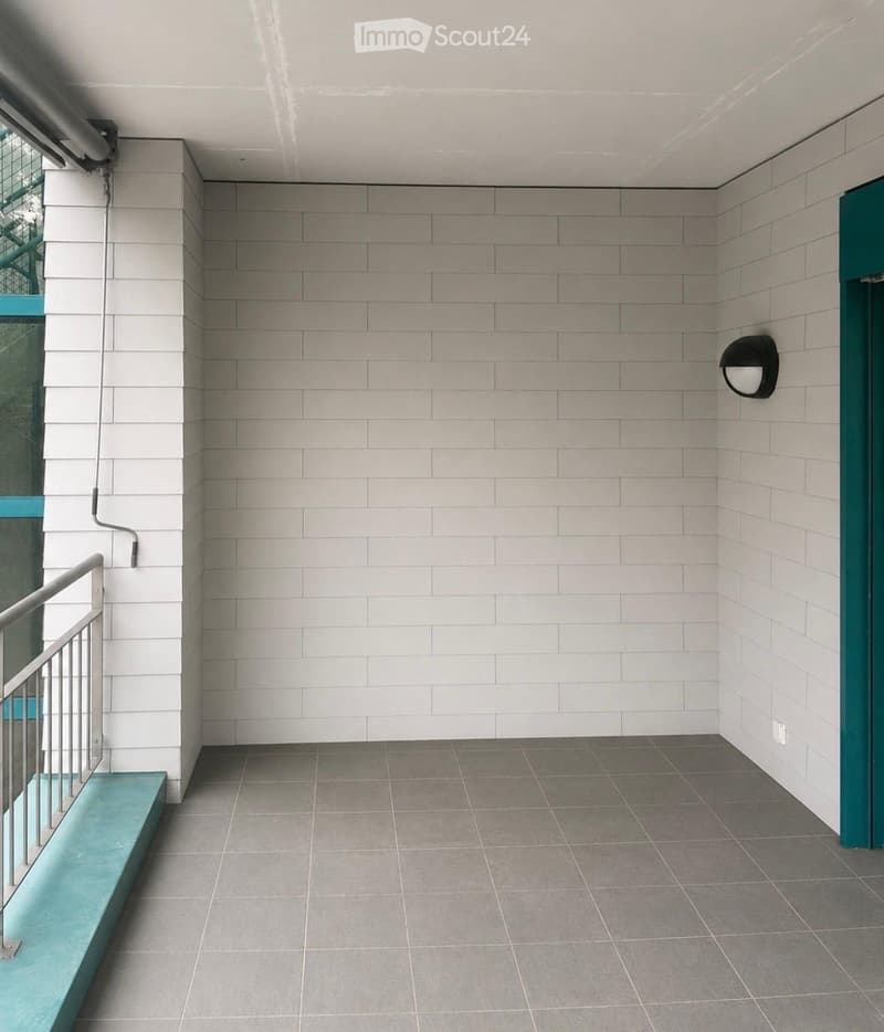 Modern hallway with grey tiled walls and floor, metal railing, and a teal-colored bench.