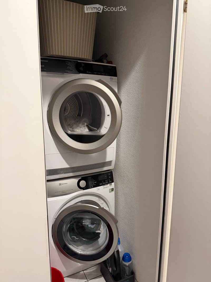 A compact bathroom with a stacked washing machine and dryer unit, featuring a control panel and a small shelf above.