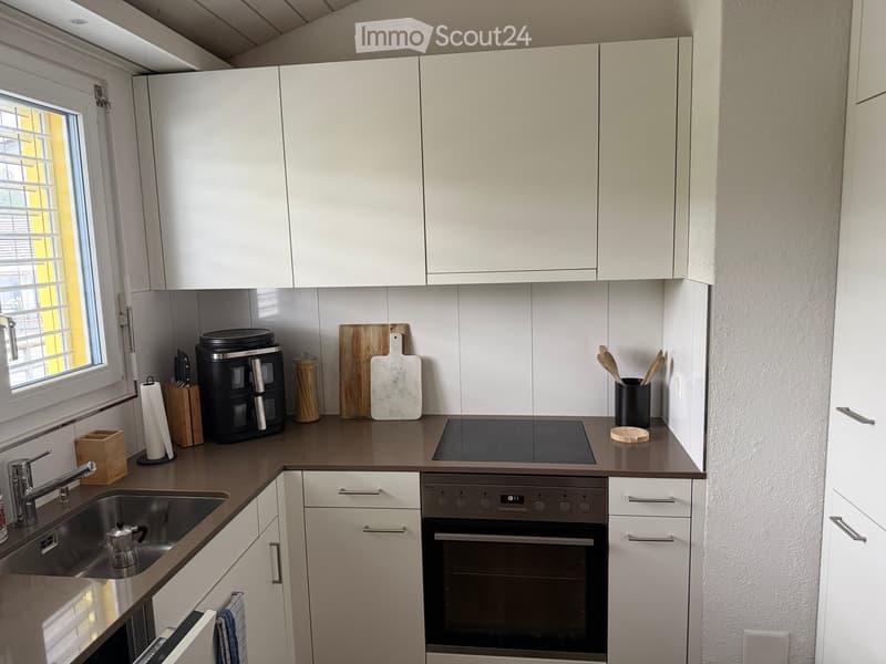 Modern kitchen with white cabinets, stainless steel sink, built-in oven, and various appliances and utensils on the counter.