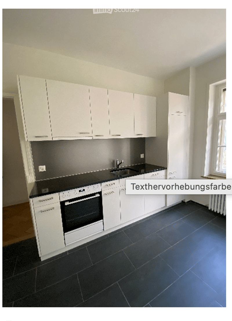 Modern kitchen with white cabinets, black countertops, and a built-in oven. Features a sink with a faucet and a window providing natural light.