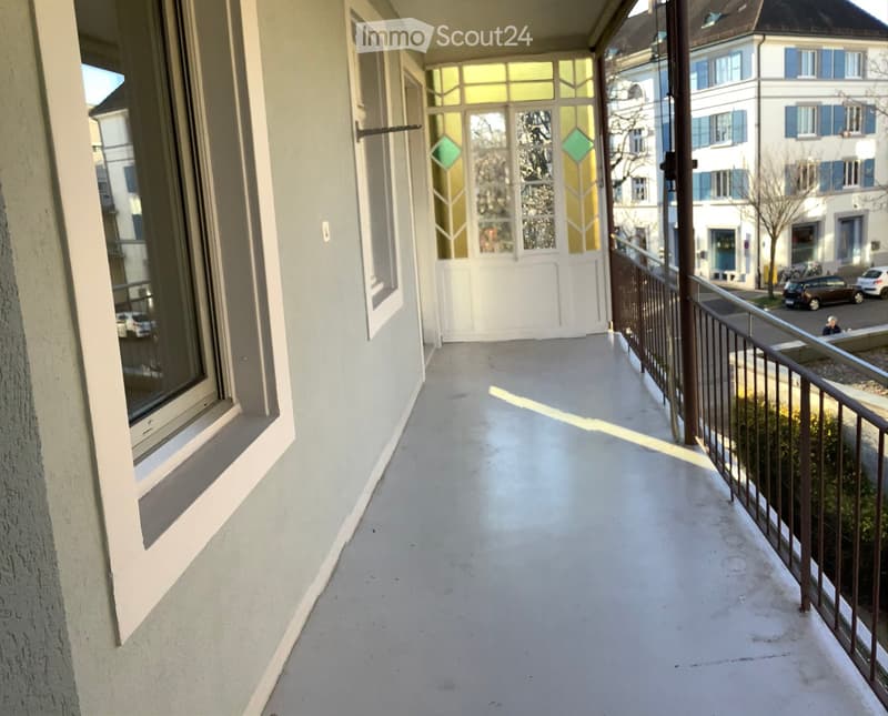 Balcony with white floor, metal railing, and large windows with decorative glass panels.