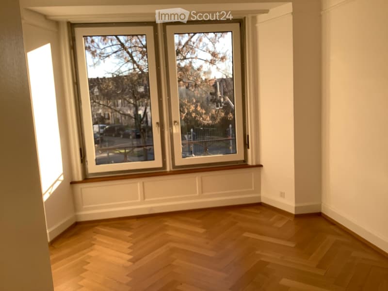Empty room with wooden flooring, large windows, and white walls.