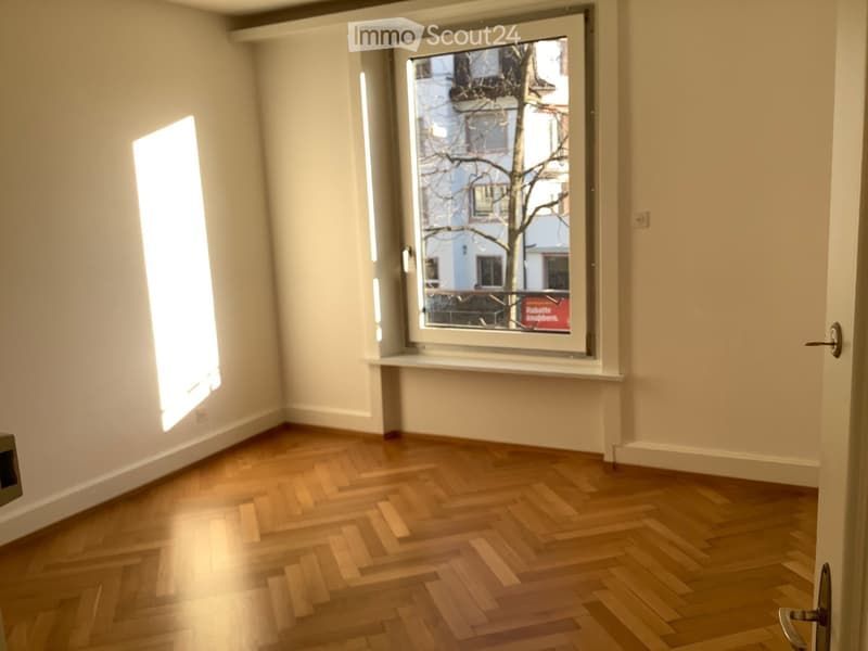 Empty room with wooden flooring, white walls, and large windows letting in natural light.