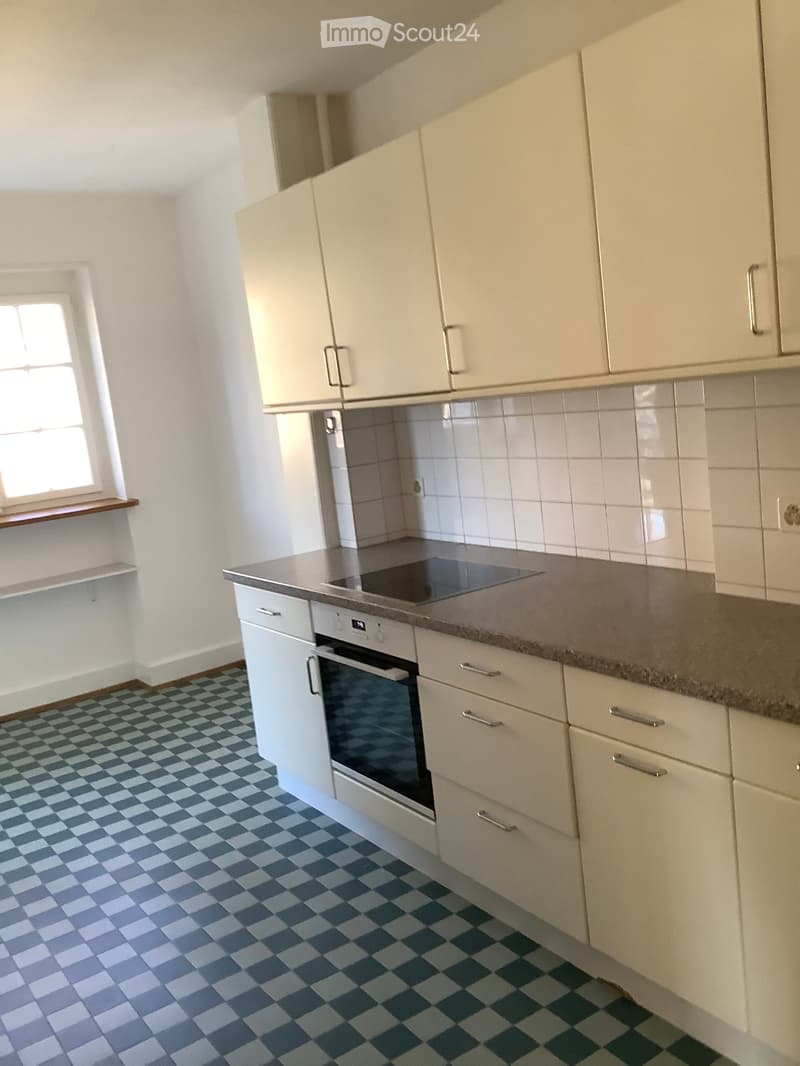 Modern kitchen with white cabinets, a built-in oven, and a grey countertop. The floor features a blue and white checkered tile pattern.