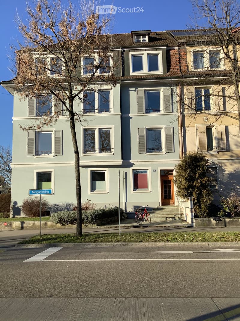 Two-story residential building with light blue and beige facade, multiple windows, and a bicycle parked in front.