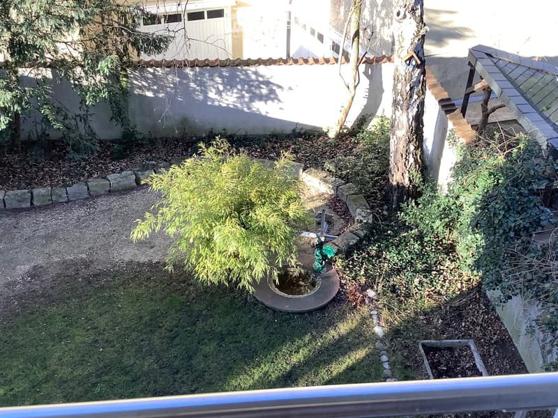 Small, enclosed garden with a tree, shrubs, a small fountain, and a gravel path.