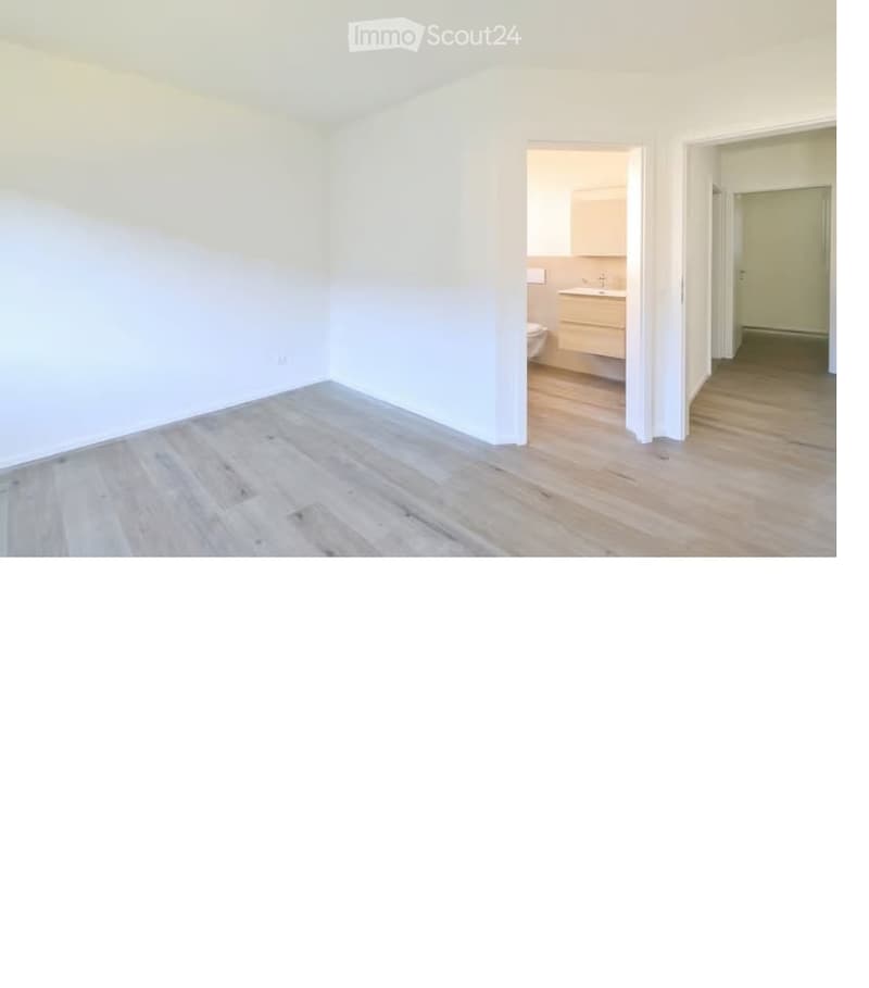 Empty room with light wooden flooring and white walls, featuring an open doorway leading to a small bathroom with a sink and toilet.