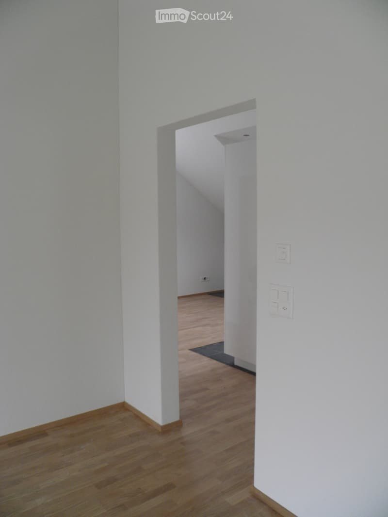 Empty hallway with light wooden flooring and white walls, featuring a small rug and electrical outlets.