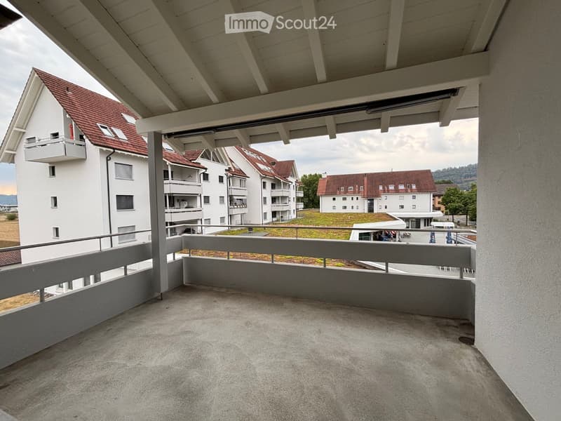 Empty balcony with concrete floor, metal railing, and a view of surrounding buildings and greenery.
