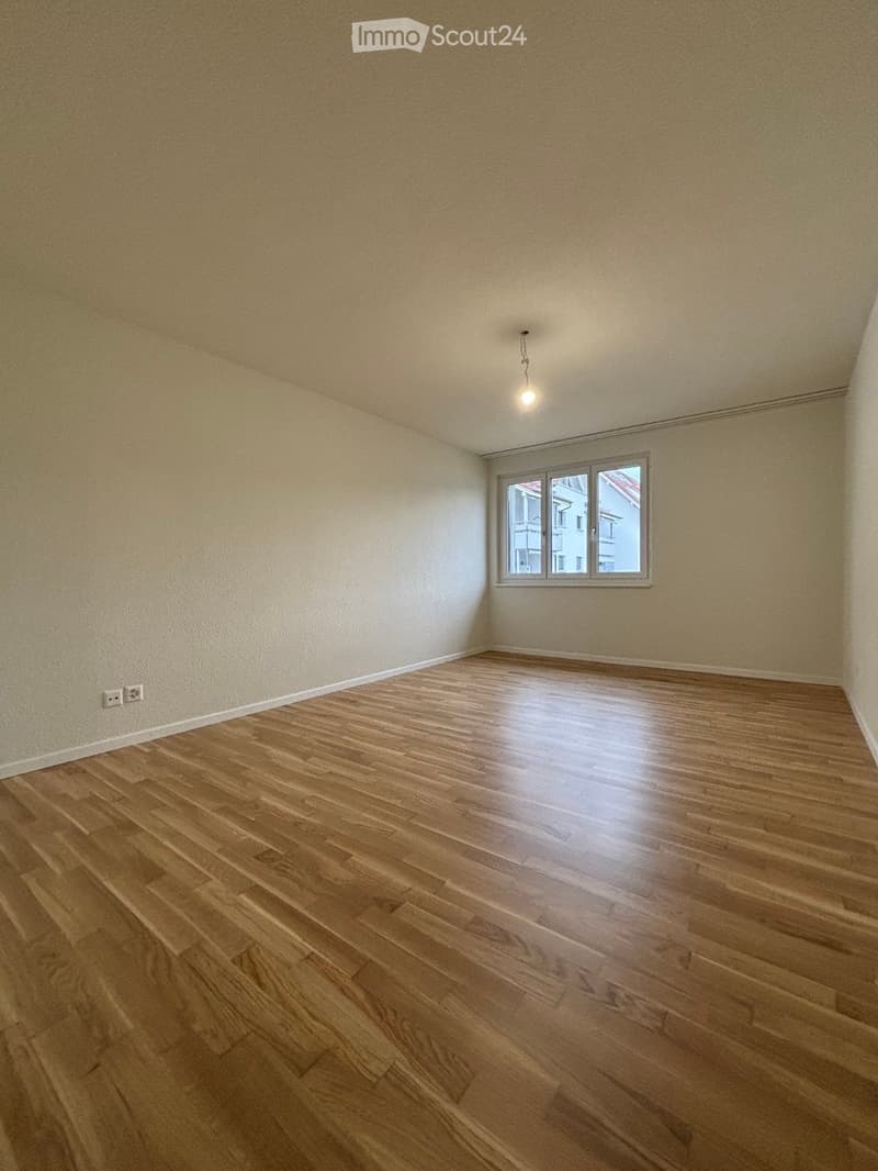 Empty room with wooden flooring and white walls, featuring a single window and a ceiling light fixture.