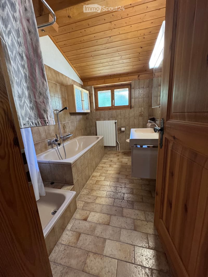 Bathroom with wooden ceiling, tiled walls, bathtub, sink, mirror, radiator, and cabinet.