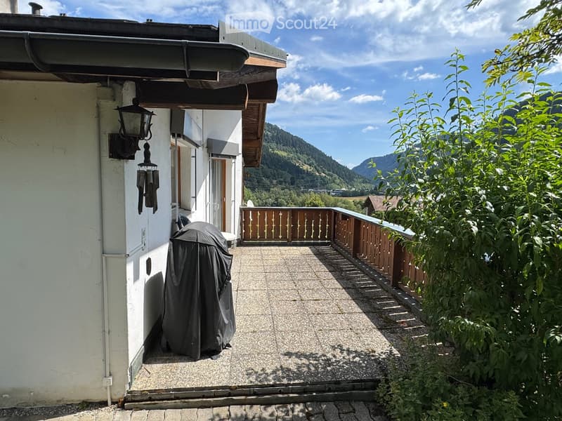 Balcony with wooden railing, covered grill, and scenic mountain view.