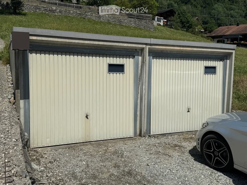 Two-car garage with light-colored doors and small windows, situated on a gravel driveway with a car partially visible.