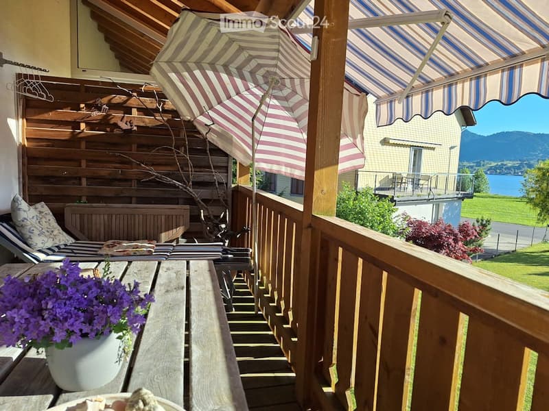 Balcony with wooden decking, striped awning, lounge chair, umbrella, and scenic mountain view.