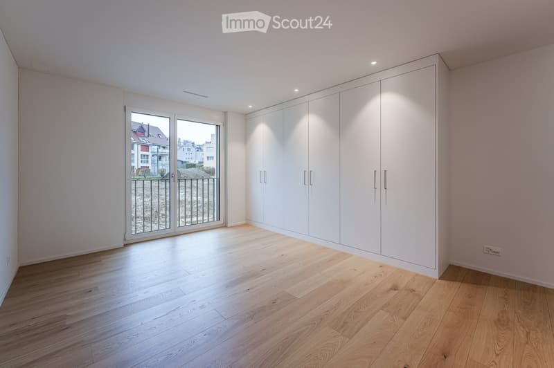 Empty room with light wooden flooring, white built-in wardrobes, and a large glass door leading to a balcony with a view of the street.