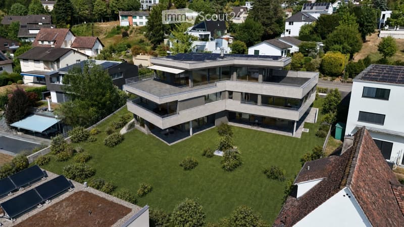 A modern, multi-story house with large windows and solar panels on the roof, surrounded by a well-maintained lawn and trees.