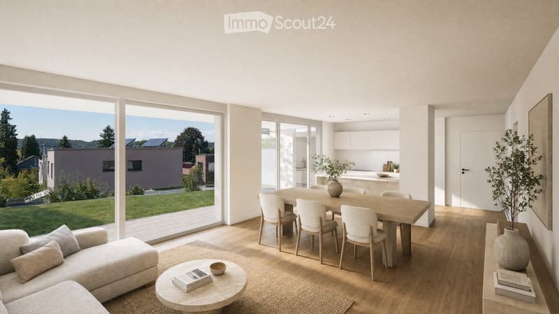 Bright, open-plan living and dining area with large windows offering a scenic view. Features a light-colored sofa, coffee table with books, a wooden dining table with chairs, and a modern kitchen area visible in the background.