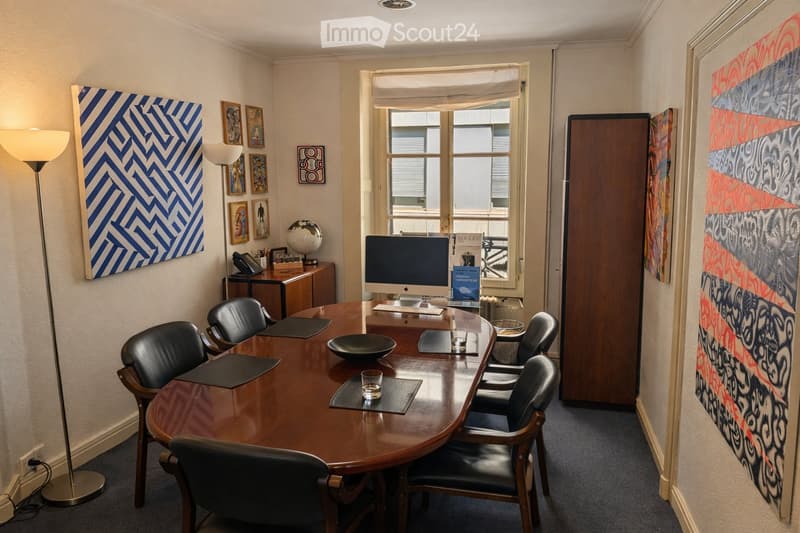 Conference room with a large wooden table, black chairs, computer, floor lamp, framed artwork, globe, and telephone.