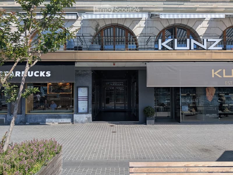 Facade of a multi-story building with storefronts including Starbucks and KLUZ, featuring large arched windows, a balcony, and a paved brick sidewalk.