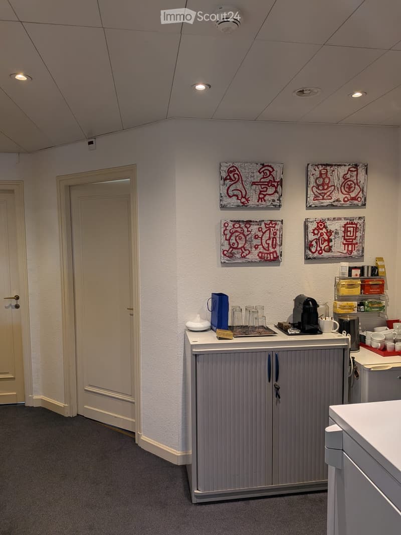 A small break room with a grey cabinet, coffee machine, cups, and a small counter area.