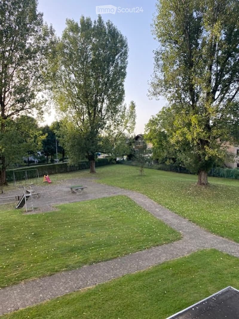 A well-maintained park area with grassy patches, a gravel pathway, and a small playground featuring swings and a slide.
