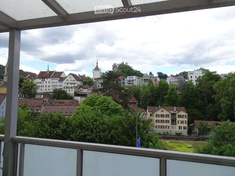 Balcony overlooking a cityscape with historic buildings, trees, and a castle on a hill.