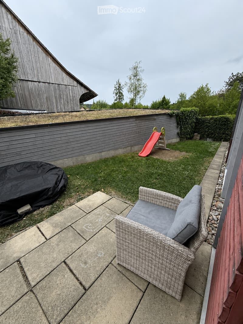 Garden area with a wicker chair, a slide, a covered object, and a wooden fence.