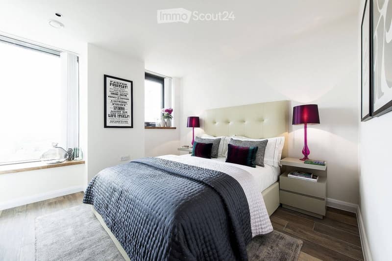 Modern bedroom with a large bed, nightstands, lamps, and decorative items on the windowsill.